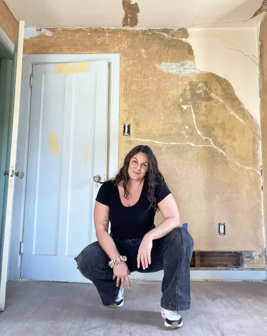 Alana crouching in a room of her house mid-renovation