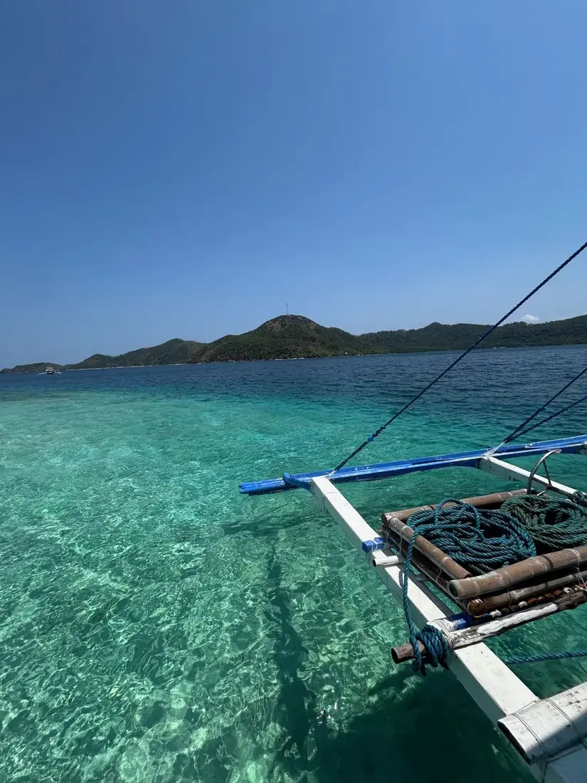 Boat outrigger over clear turquoise water while island hopping