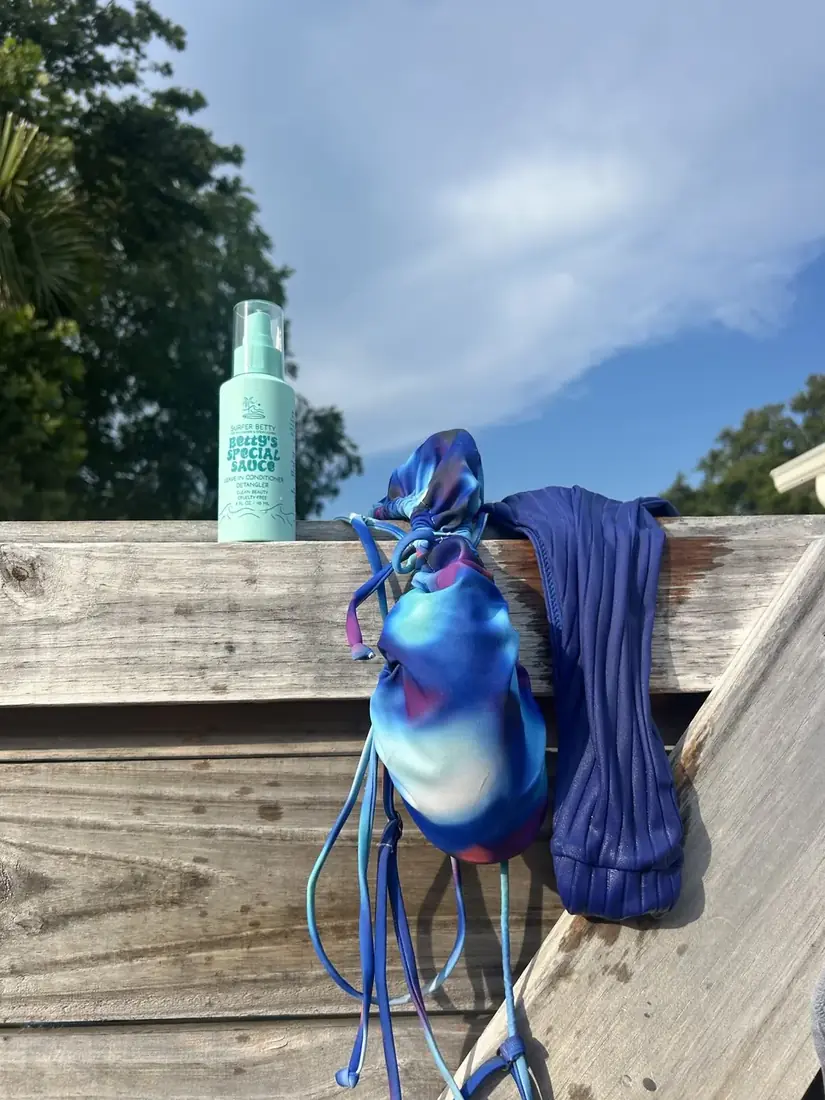 Surf Betty bikini and skincare on a sunny wooden fence