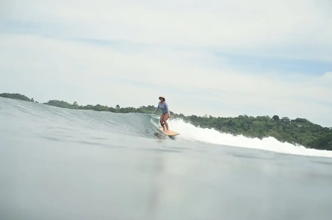 Alana riding a wave with jungle behind